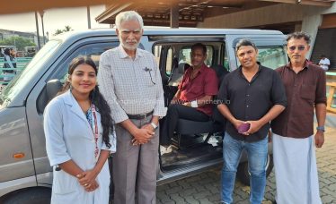 A close-up photograph of 73-year-old Mohanan looking weary but relieved, sitting at the Kuttippuram railway station while local social workers and Selva Care coordinators stand supportively beside him during his rescue.