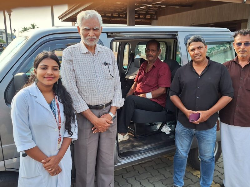 A close-up photograph of 73-year-old Mohanan looking weary but relieved, sitting at the Kuttippuram railway station while local social workers and Selva Care coordinators stand supportively beside him during his rescue.